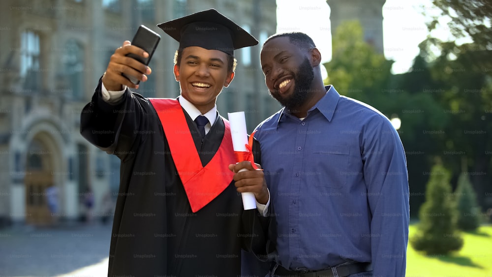 Feliz manto de graduación de estudiante universitario y padre tomando selfie smartphone