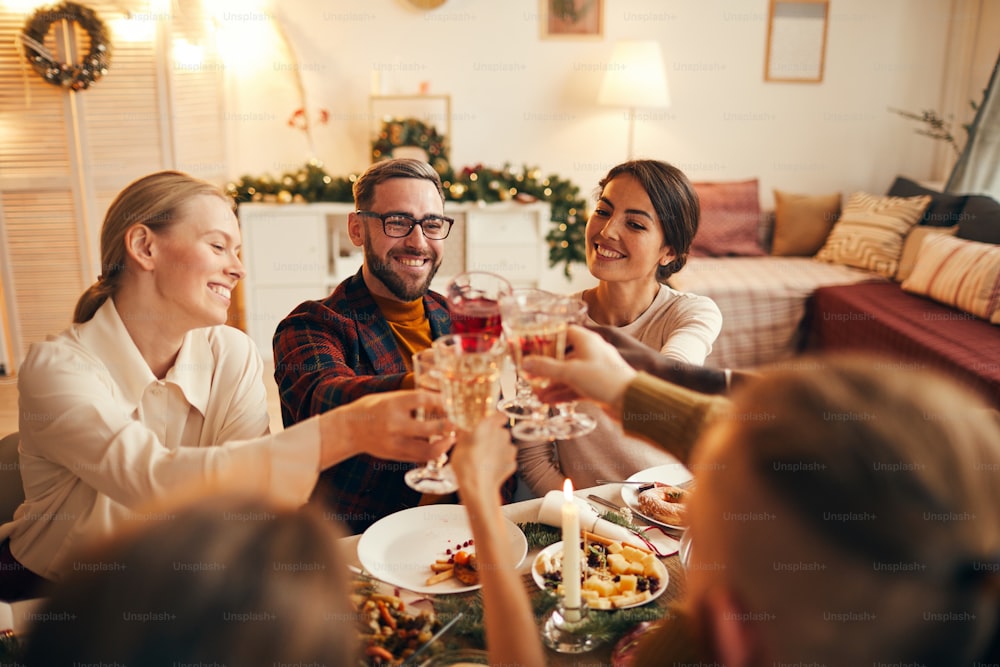 Retrato de alto ángulo de personas adultas alegres tintineando copas de champán mientras disfrutan de la cena de Navidad en casa, copiar espacio