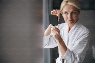 Attentive woman making shape for her eyebrows, using tweezers