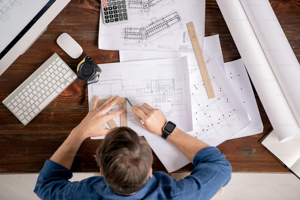 Visão geral do engenheiro ocupado com régua e lápis sentado à mesa e linha de desenho no esboço da construção arquitetônica