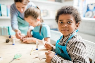 Diligent African schoolboy in blue apron preparing handmade carton halloween decorations at lesson