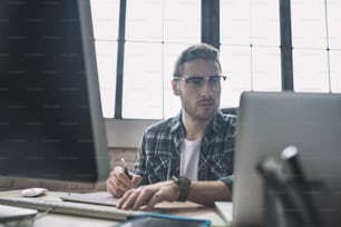 Getting drafts ready. Young bearded man in eyeglasses drafting schemes