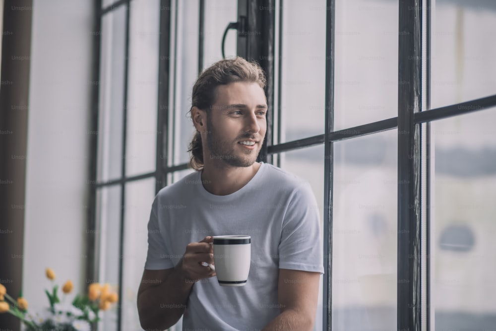 Morning drink. Inspired and energetic long-haired man having a cup of morning coffee.