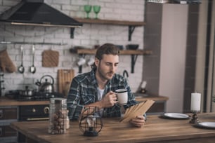 Coffee and readings. Concentrated young man reading old cards at his kitchen