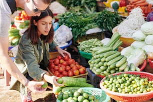 Pareja viajera comprando tomates frescos y limas en el mercado local con productos orgánicos
