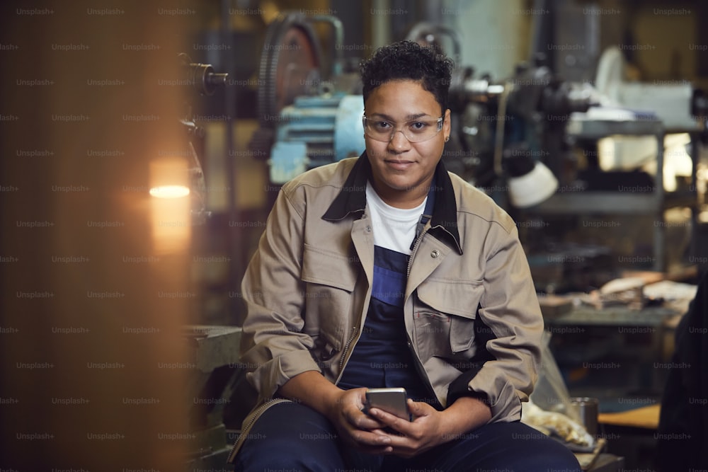 Portrait of contemporary mixed-race woman smiling at camera while posing in factory workshop