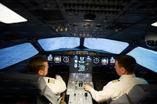Vue arrière de pilotes concentrés sérieux en chemises blanches avec rayures assis au panneau de commande de l’avion et se préparant au vol