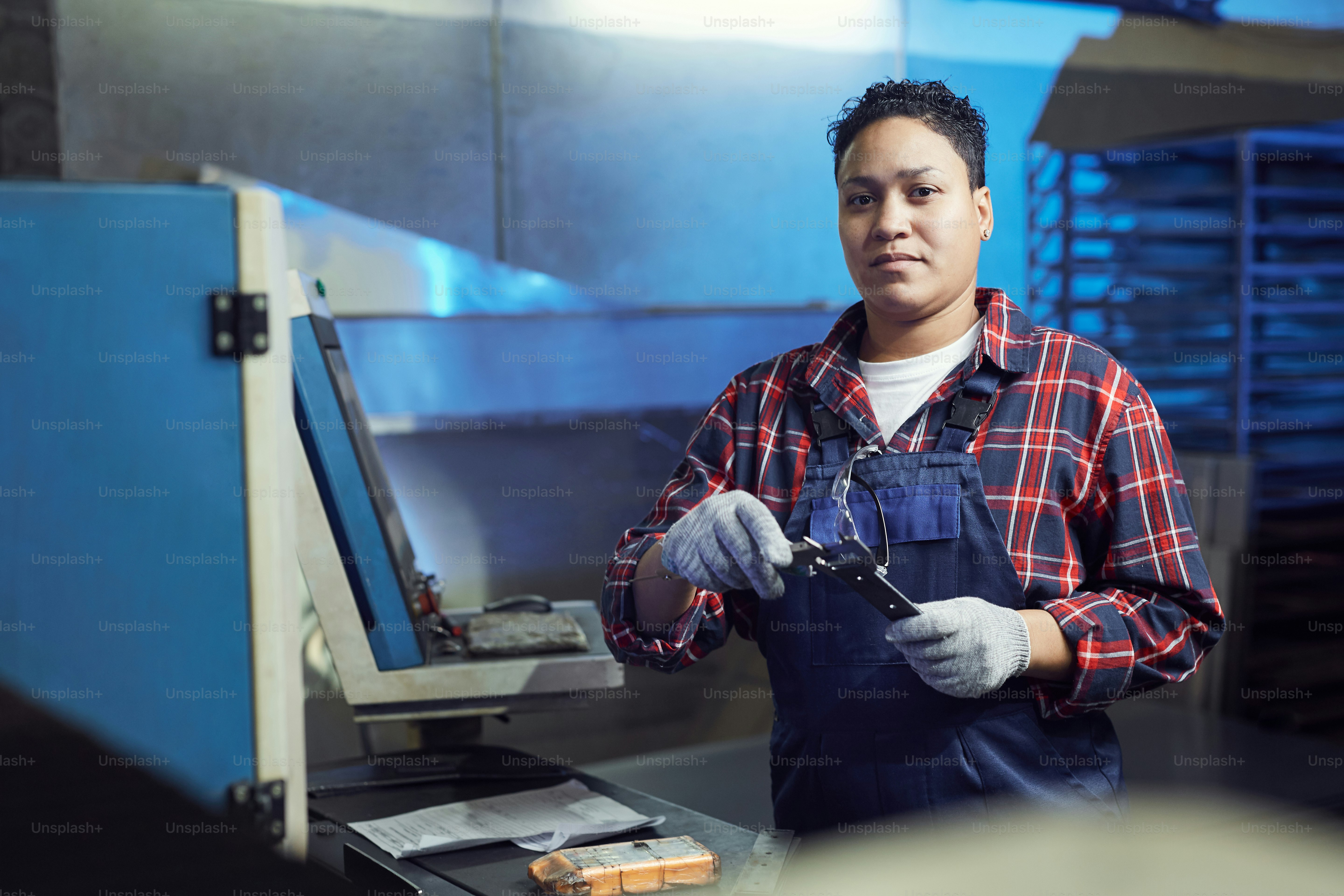 Waist up portrait of mixed-race female worker looking at camera while standing by control panel in factory workshop, copy space