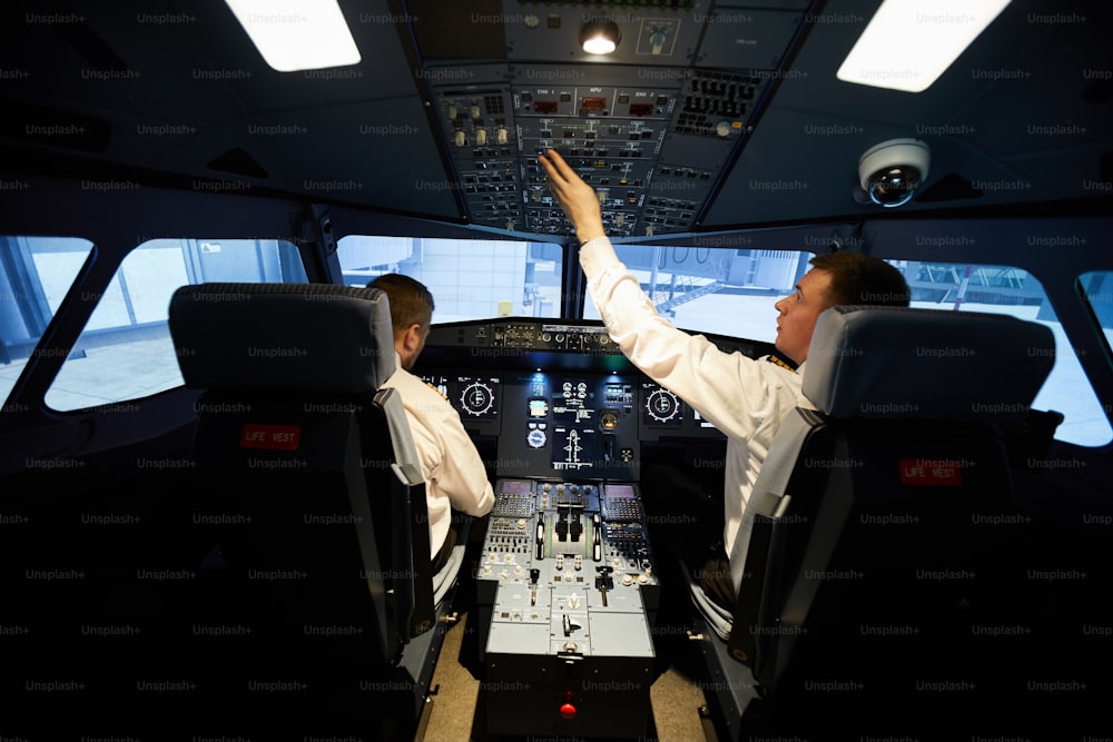 흰 셔츠를 입은 진지하고 바쁜 젊은 비행사들이 비행기 대시보드에 앉아 비행 전 준비를 하는 뒷모습