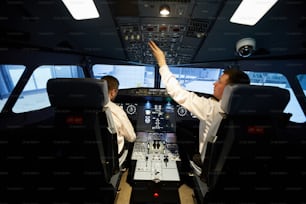 Rear view of serious busy young aviators in white shirts sitting at airplane dashboard and making pre-flight preparation