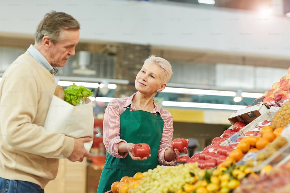 Porträt einer lächelnden älteren Frau, die Obst und Gemüse an Kunden verkauft, während sie auf dem Markt arbeitet, Kopierraum