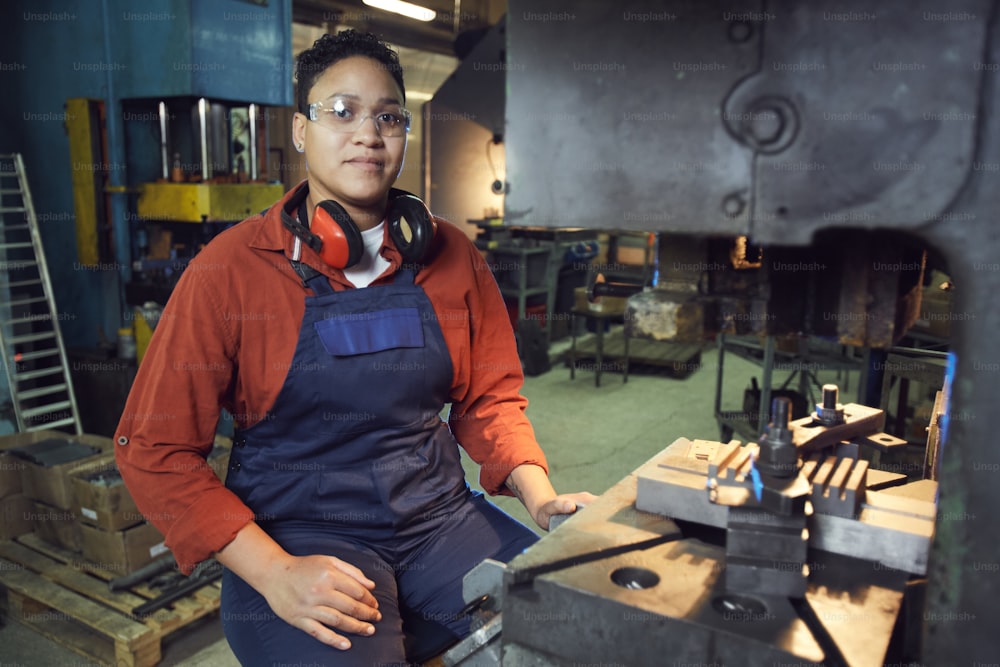 Porträt eines gemischtrassigen Fabrikarbeiters, der in die Kamera schaut, während er mit industriellen Maschineneinheiten in der Werkstatt posiert, Kopierraum