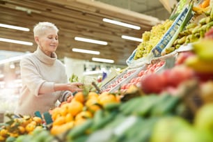 Retrato de cintura para arriba de una mujer adulta sonriente que elige verduras frescas mientras compra comestibles en el mercado de agricultores, copie el espacio