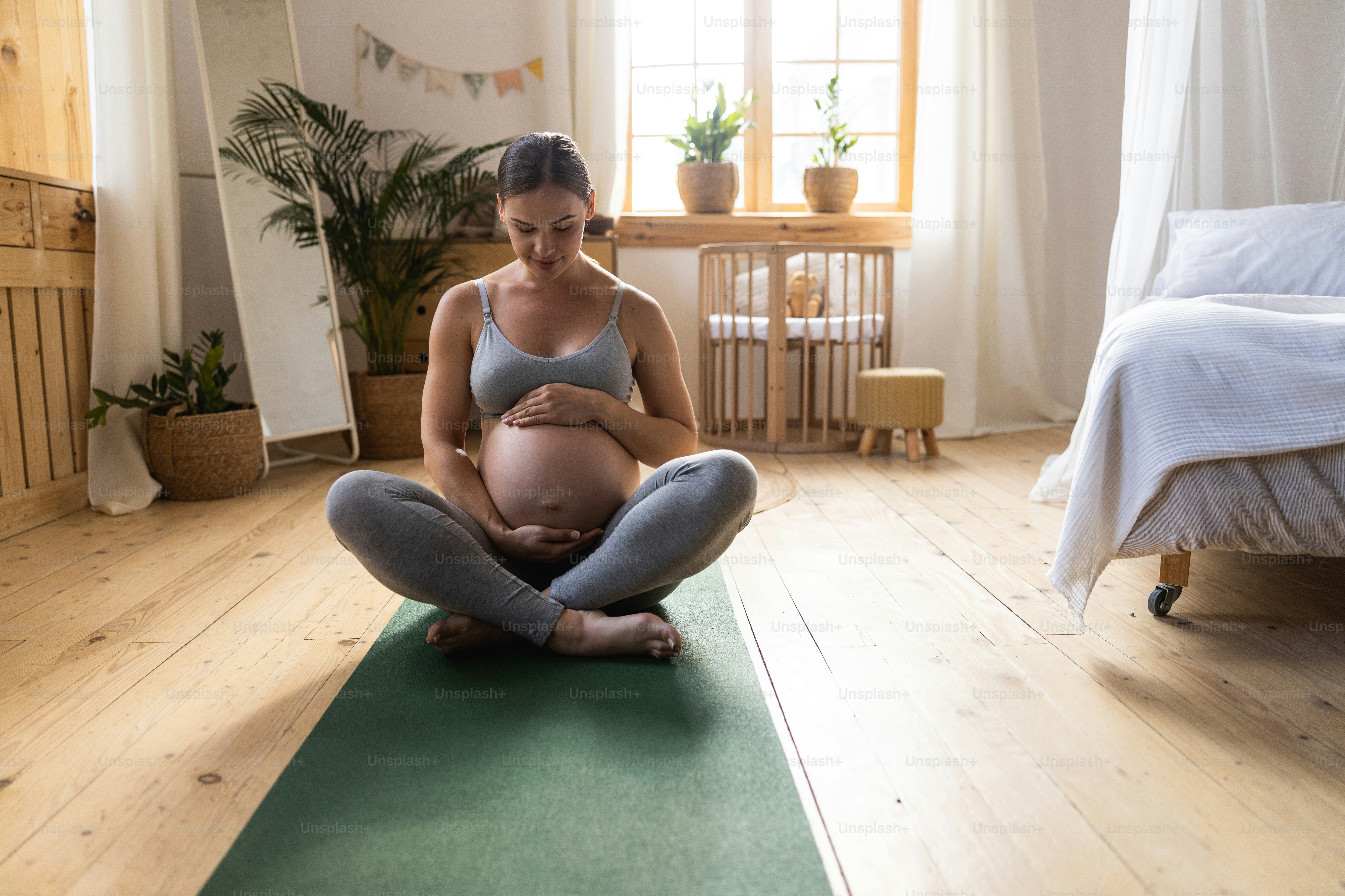 Young pregnant lady sitting on mat in her room stock photo