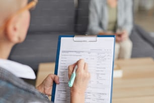 High angle closeup of female psychologist filling in medical form while talking to patient during therapy session, copy space