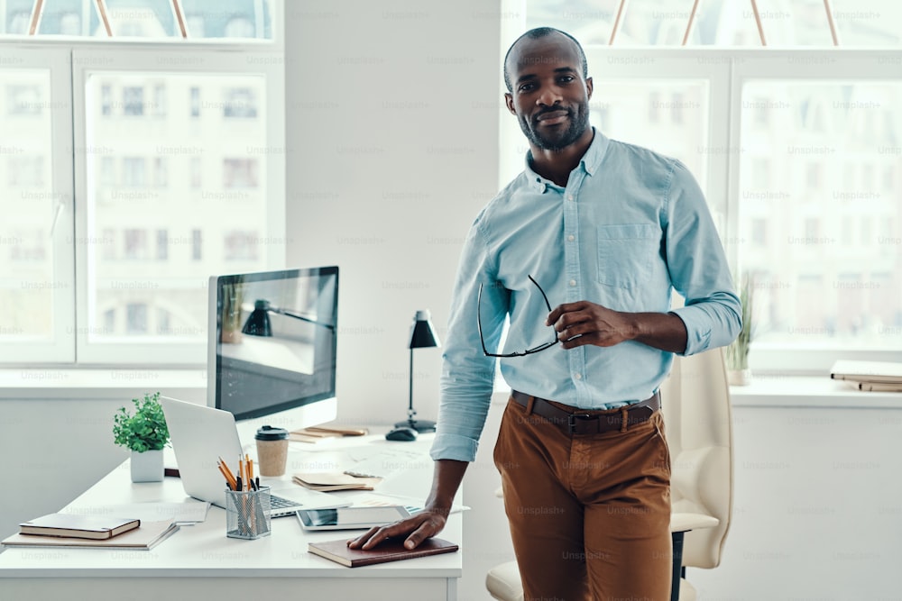 Happy young African man in shirt looking at camera and smiling while working in the office