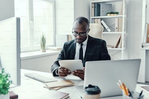 Concentrated young African man in formalwear using modern technologies while working in the office