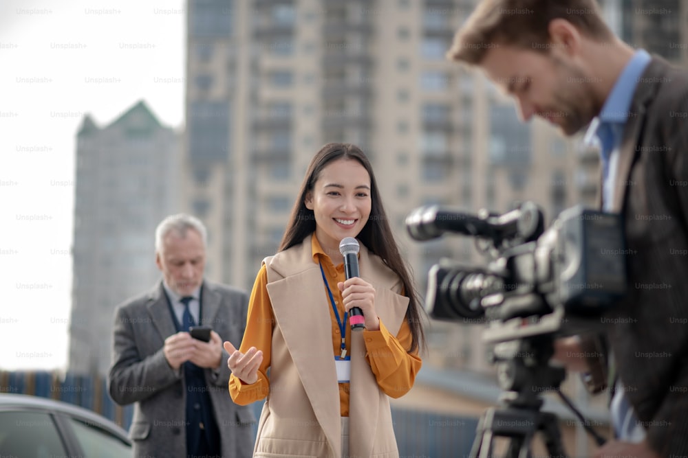Live. Young cute female reporter in a beige outfit talking to a videocamera