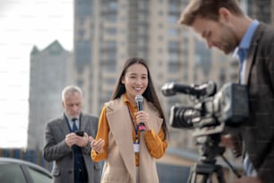 Live. Young cute female reporter in a beige outfit talking to a videocamera