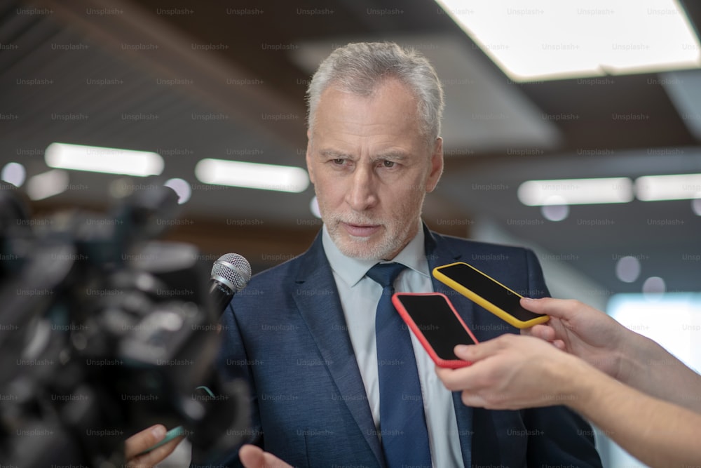 Meeting media. Grey-haired bearded man looking serious while having the press conference