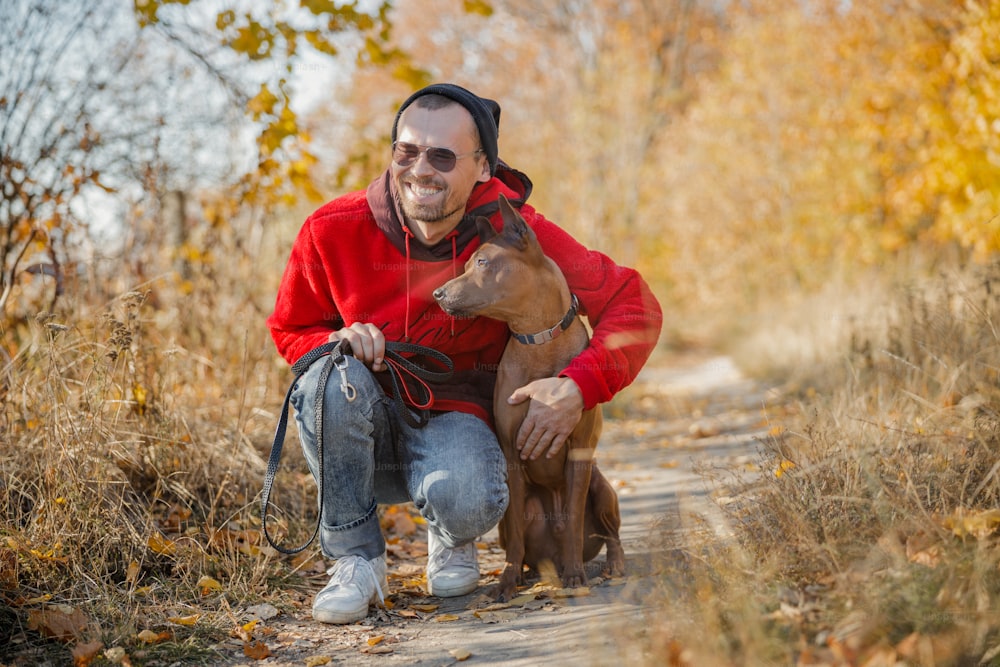 Positive young owner smiling happily while hugging his dog in the forest