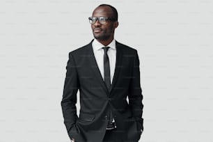 Giovane uomo africano fiducioso in abiti formali che distoglie lo sguardo mentre si trova su sfondo grigio
