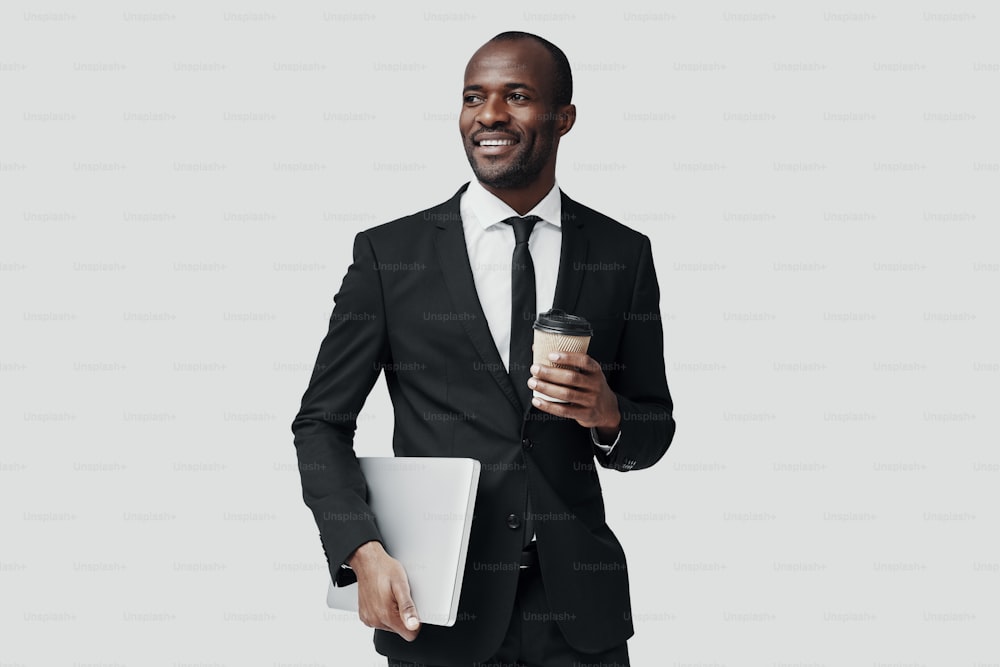 Glücklicher afrikanischer Mann in formeller Kleidung, der wegschaut und lächelt, während er vor grauem Hintergrund steht