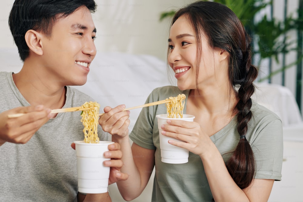 Gli studenti universitari mangiano spaghetti istantanei da bicchieri di plastica con le bacchette e si guardano l'un l'altro