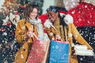 Due giovani donne multietniche attraenti che reggono borse della spesa e sorridono. . Lo sfondo è la decorazione di Capodanno