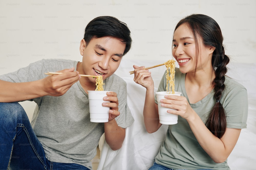 Giovane coppia vietnamita felice che mangia gustoso ramen da bicchieri di plastica