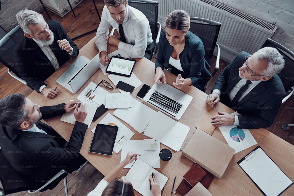 Vista dall'alto di colleghi in eleganti abiti formali che discutono dei rischi aziendali mentre lavorano nell'ufficio moderno