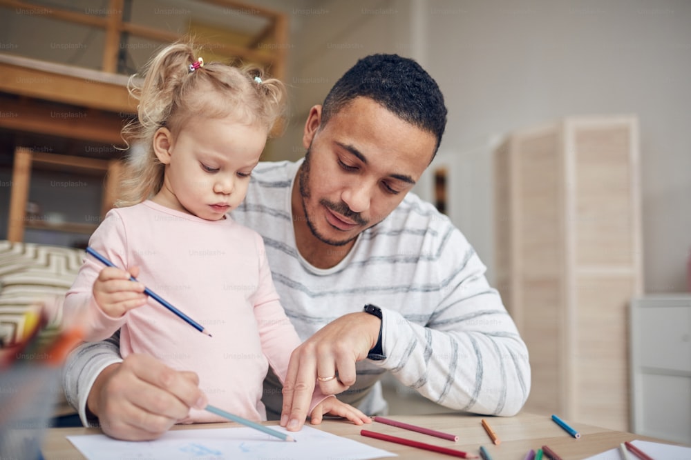 Portrait of contemporary father drawing pictures together with cute little daughter at home, copy space