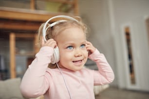 Retrato de cintura para arriba de una linda chica de ojos azules con auriculares grandes y disfrutando de la música en el interior de la casa, espacio de copia