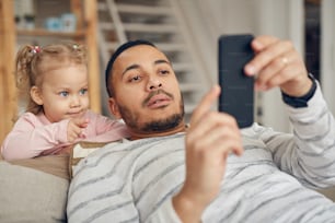 Portrait of young father showing smartphone games to cute little daughter at home, copy space