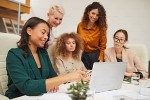 Group of five attractive female office workers watching something on laptop during business meeting