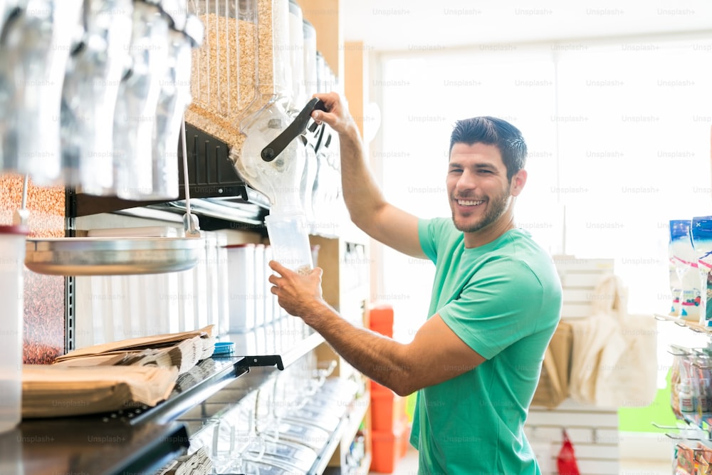 Retrato do homem sorridente servindo comida no recipiente enquanto compra a granel no supermercado