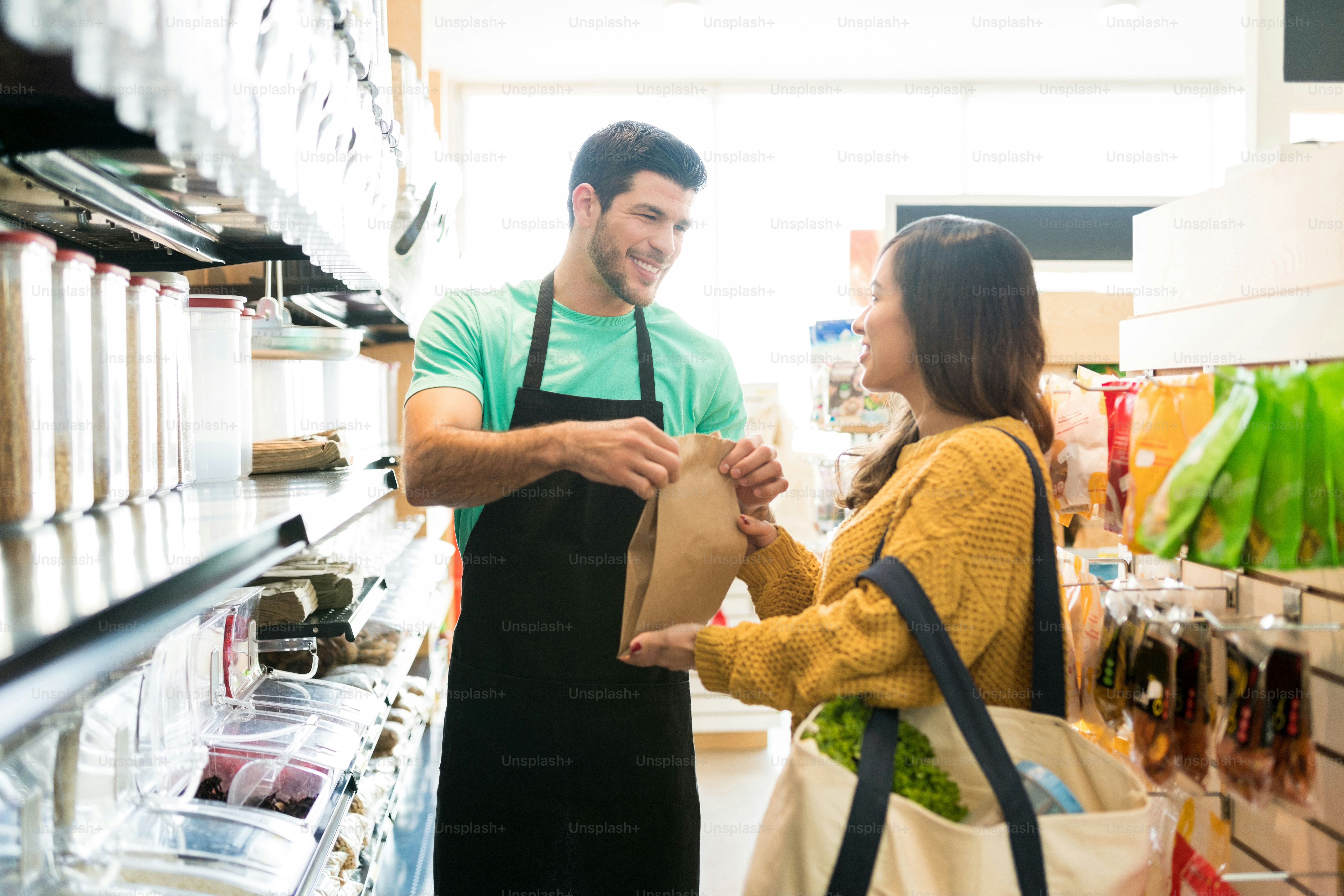Smiling male owner giving paper bag to female customer and selling food in bulk in supermarket