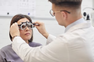 Ritratto di giovane oculista che mette la cornice di prova sulla paziente femminile durante il controllo della vista in una clinica moderna, spazio di copia