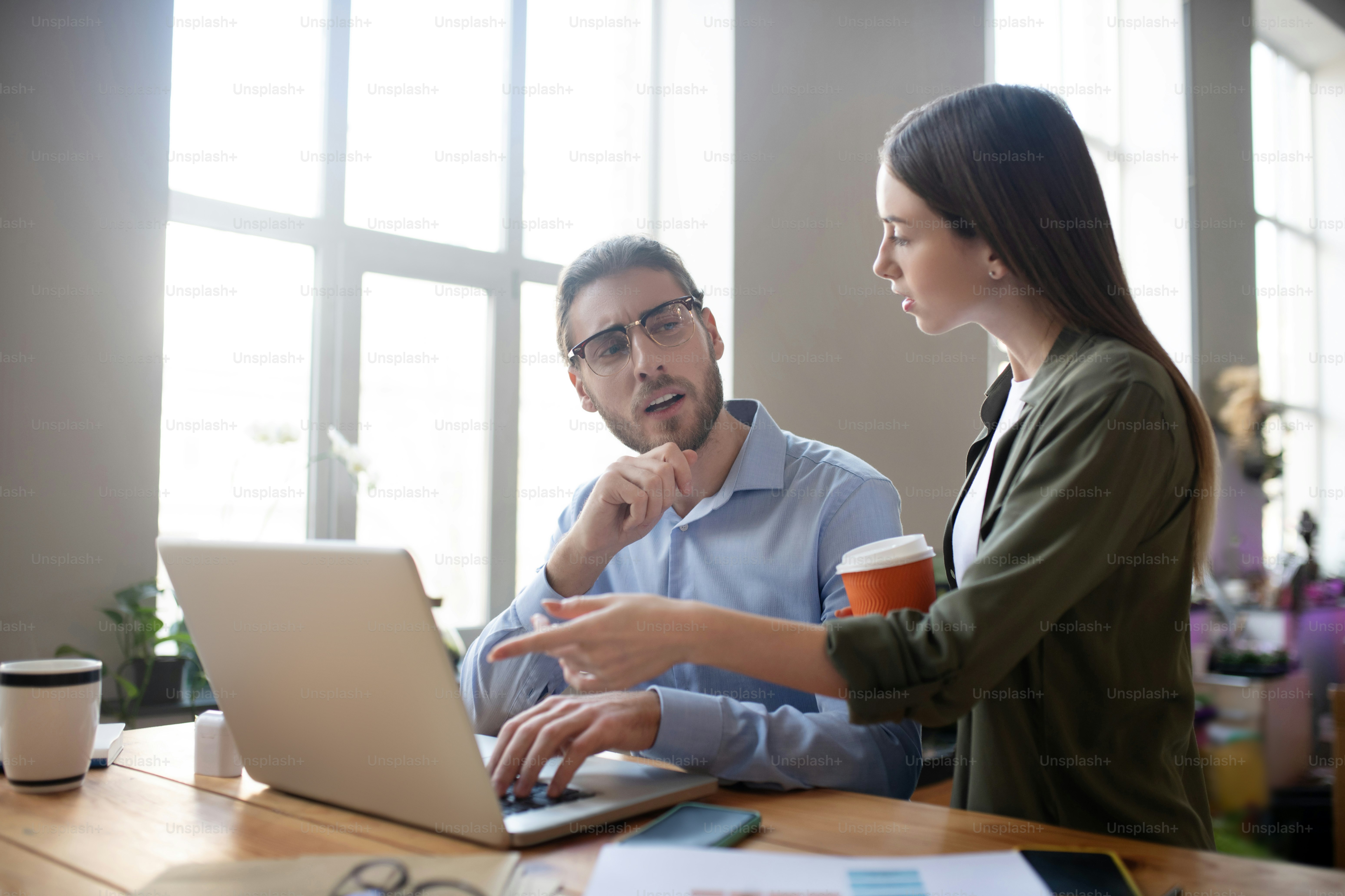 공동 사업 프로젝트. 커피 한 잔을 든 소녀와 안경을 쓴 남자가 노트북 근처의 테이블에 앉아 공동 사업 프로젝트를 논의하는 두 사람 모두 진지하고 흥미 진진합니다.