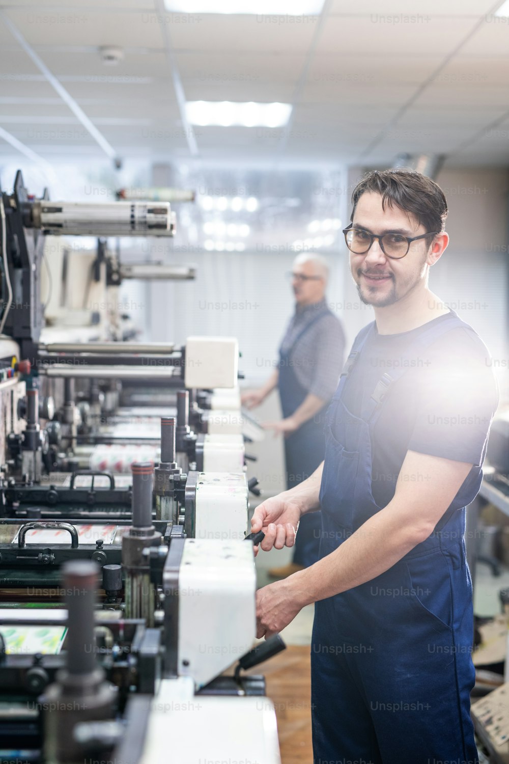Portrait of smiling young bearded man in glasses working at production line of printing plant
