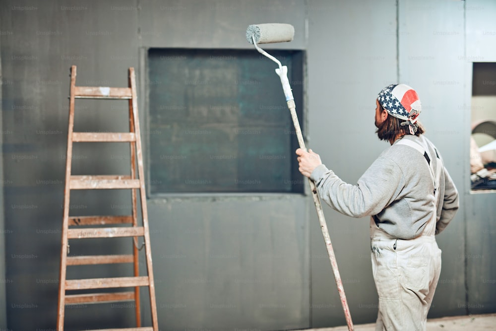 Pintor pintando paredes con un rodillo extensor en interiores.