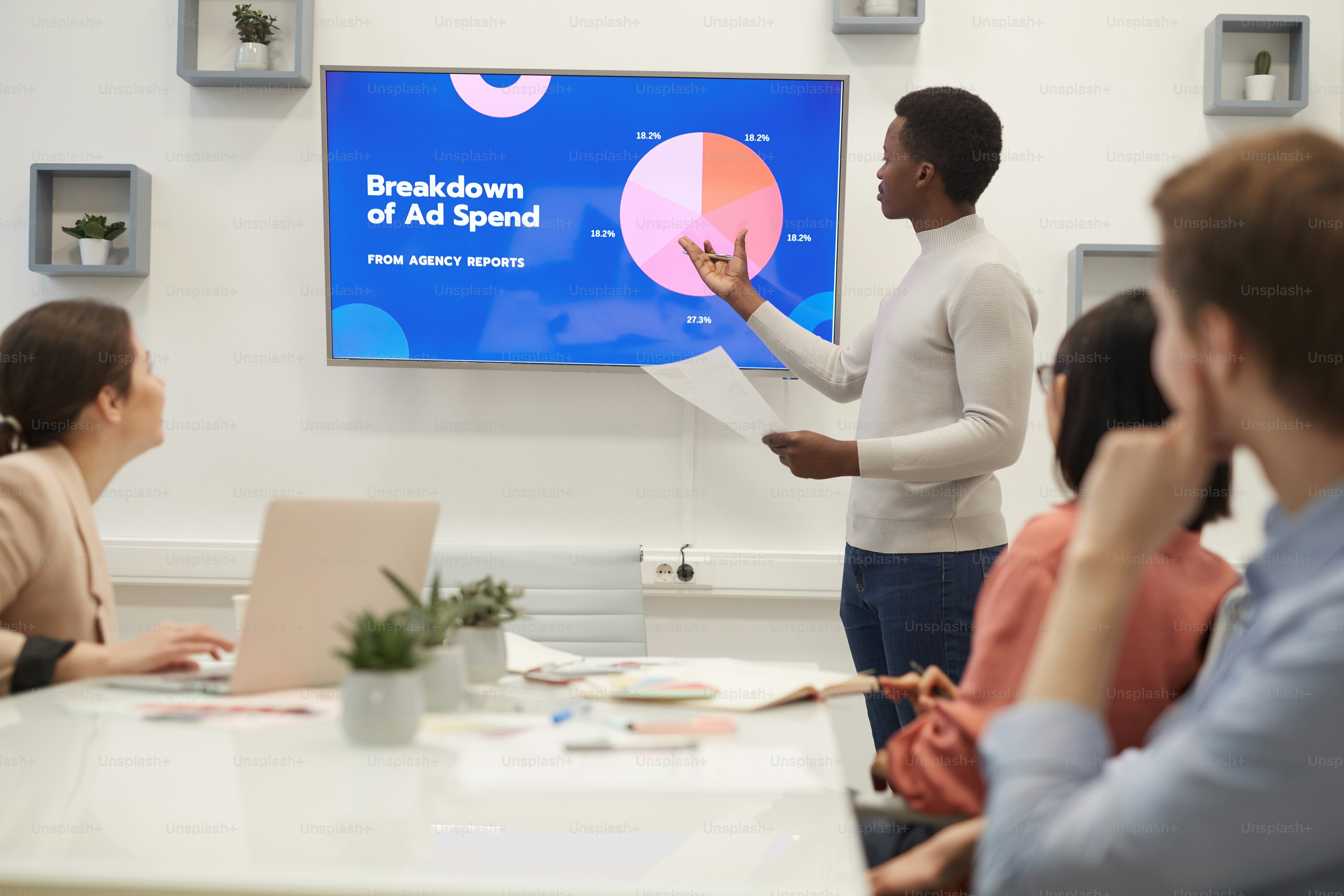 Portrait of young African businessman pointing at marketing data chart while giving presentation during meeting in modern office, copy space