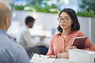 Porträt einer jungen asiatischen Geschäftsfrau, die mit einem Chef oder Manager spricht, während sie in einem modernen Bürointerieur, Kopierraum steht