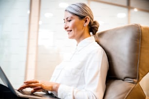 Mulher positiva em seu local de trabalho digitando letras no laptop e sorrindo