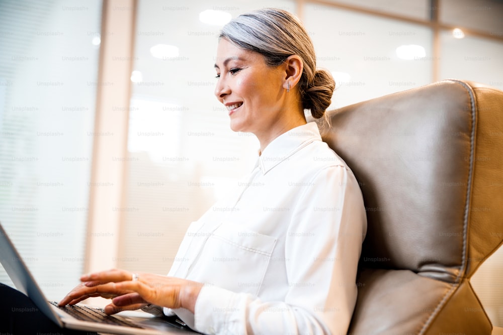 Positive woman at her workplace typing letters on the laptop and smiling
