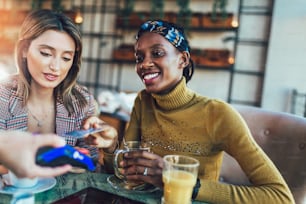 Des amis heureux utilisant une carte de crédit et effectuant un paiement sans contact dans un restaurant.