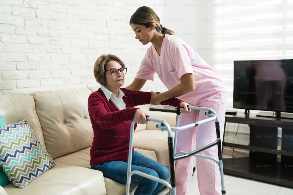 Nurse helping elderly disabled woman to walk with mobility walker at home