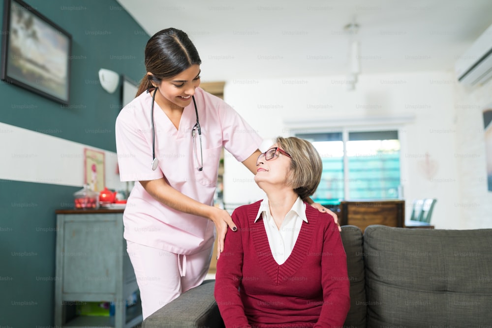 Smiling young nurse talking with senior woman sitting on sofa at home