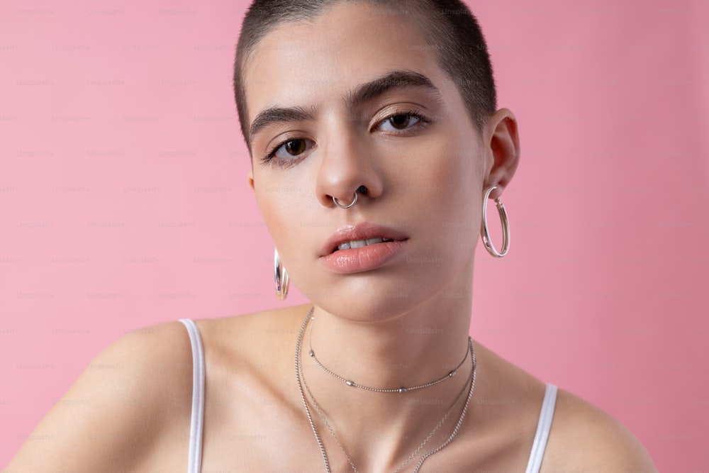Porträt eines kurzhaarigen Mädchens auf rosa Hintergrund. Silbernes Piercing in Ohren und Nase