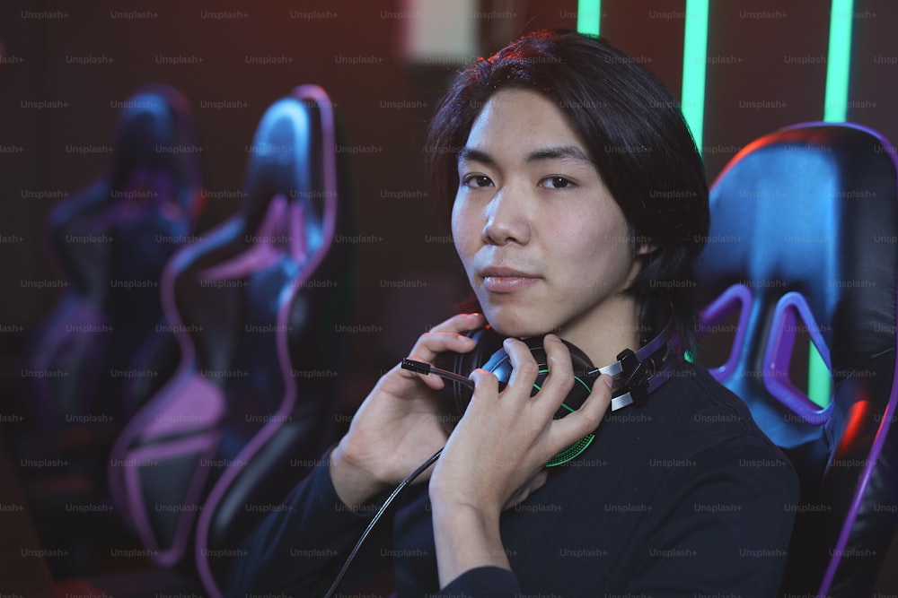 프로 게임 스튜디오에서 비디오 게임을 하는 동안 카메라를 보고 있는 젊은 아시아 남성의 초상화, 복사 공간